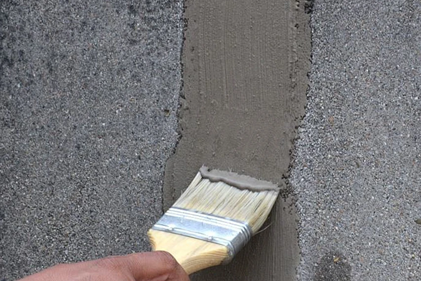 Brush applying repair mortar on a concrete surface with HEMC support